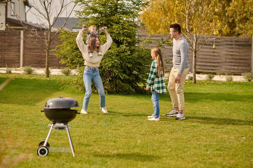 A family playing in the backyard beside a barbecue